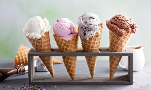 Quatre cornets de glace avec des saveurs différentes sur un support.